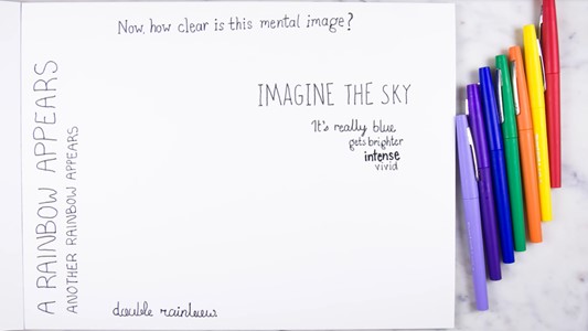 white paper notepad with handwriting: 'How clear is this mental image? Imagine the sky. it's really blue. gets brighter. intense, vivivd. a rainbow appears. another rainbow appears. double rainbow'. to the right of the notepad seven coloured pencils lay arranged ascendingly.