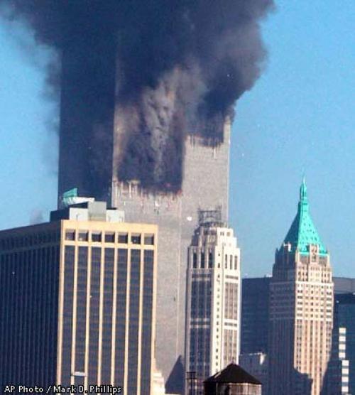 News photograph from the 11th of September 2001 terrorist attack on the World Trade Centre towers: tall skyscrapers from foreground are dwarfed by a much taller block of 2 skyscrapers emitting smoke from two different points. In the fluffy rolling swathes of grey smoke, a satanic face with angular chin and nose, and narrow eyes, can be made out.