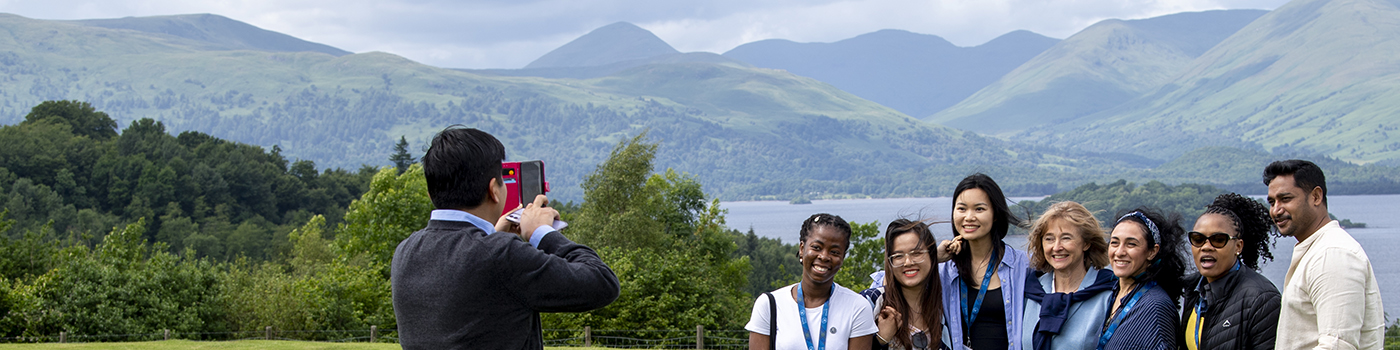 Students standing for a group photo on a grassy slow with views of the hills and the sea at Dumfries